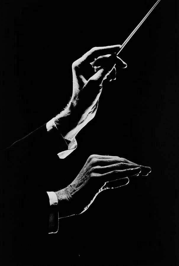 تصویری سیاه و سفید از دستان رهبر ارکستر در حال هدایت ارکستر، همراه با عصا، که به آن «باتون» می‌گویند.